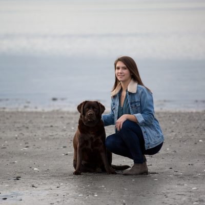 High School Senior portrait. Using natural light in a fashion inspired style. Women on beach with her dog.