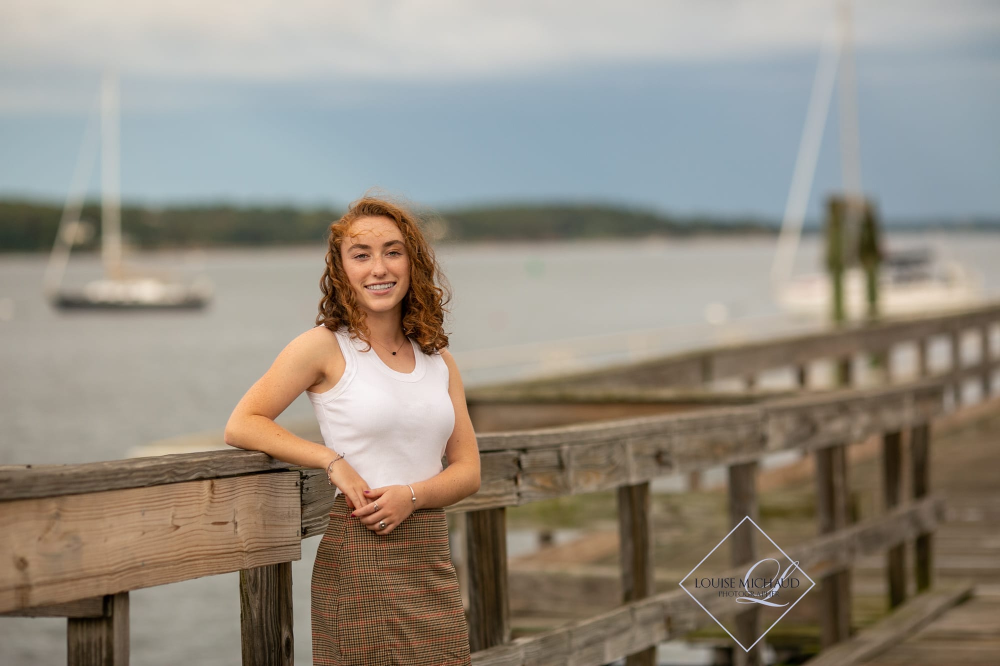 High School Senior portrait. Using natural light in a fashion inspired style. Lighthouse in background. Hair blowing in the wind on a dock by the sea.